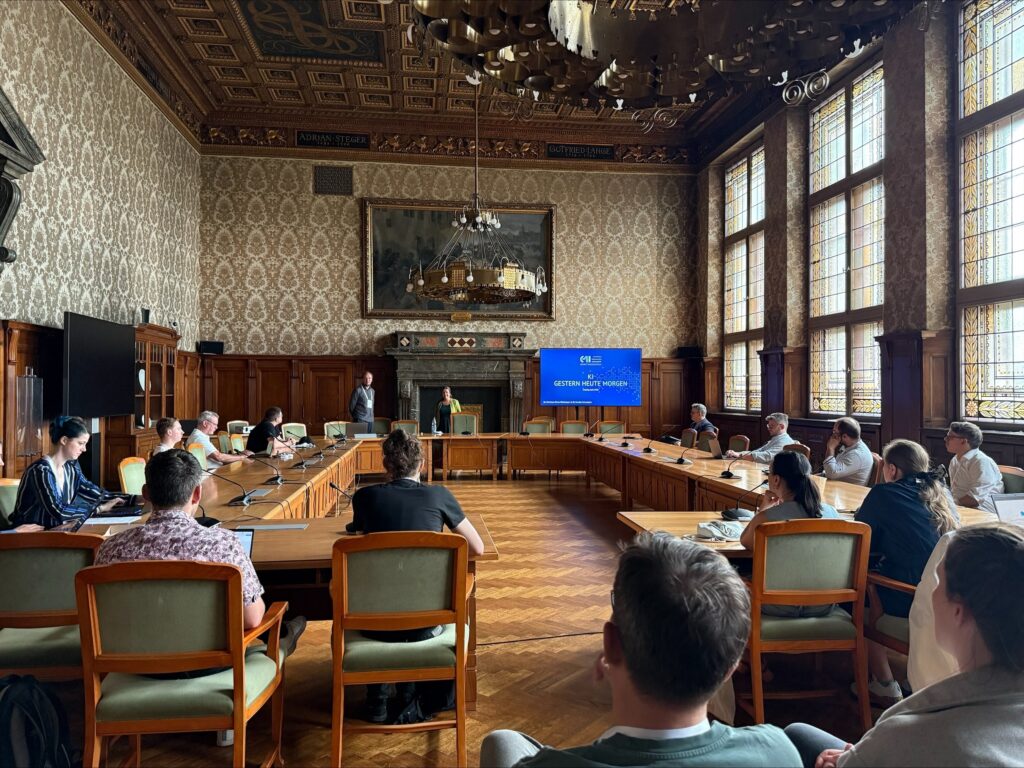 Workshopsetting im Ratsplenarsaal. Titelfolie zu sehen "KI gestern, heute, morgen"